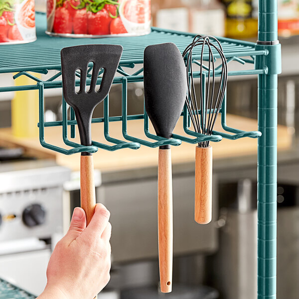 A hand holding a Regency green epoxy utensil holder with a spatula and whisk inside.