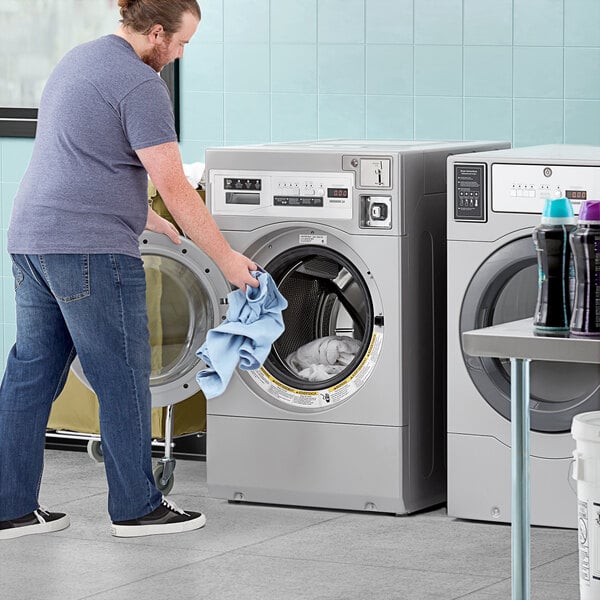 A man loading a blue towel into a Crossover commercial washer.