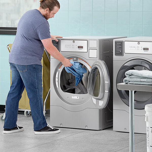 A person putting clothes into a Crossover commercial dryer.