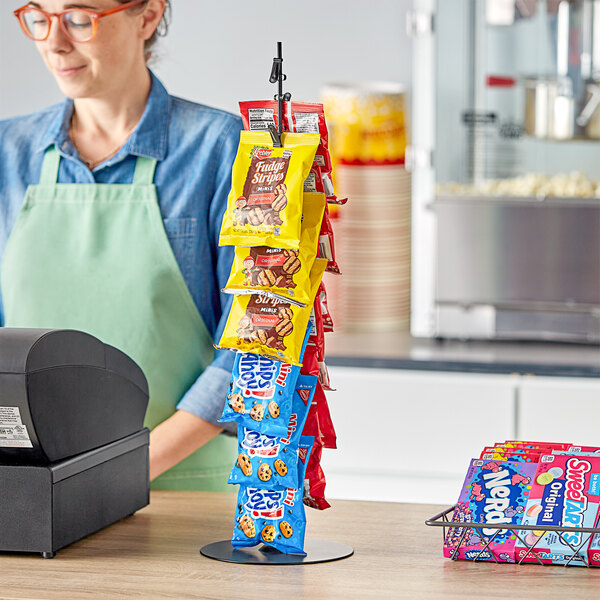 A woman behind a convenience store counter with a wire rack of candy bars.