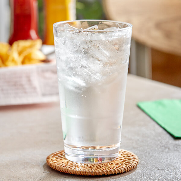 A glass of ice water with a straw on a coaster.