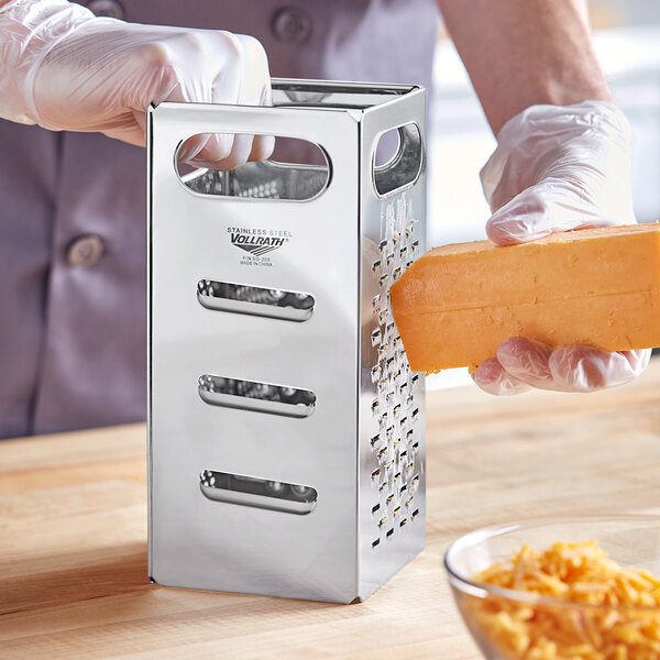 A person grating cheese on a Vollrath stainless steel box grater.