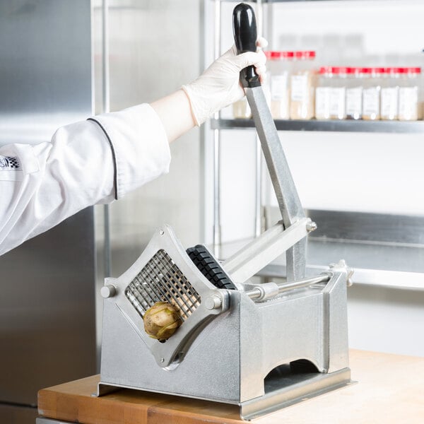 A person in a white coat and gloves uses a Nemco Monster FryKutter to slice a potato.