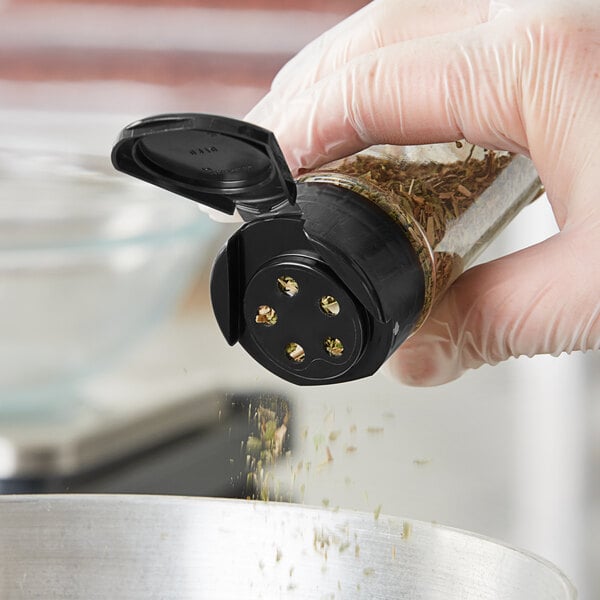 A hand using a 43/485 black flip and sift spice lid to pour seasoning into a container.