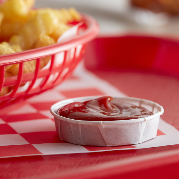 A bowl of ketchup and french fries in a Genpak Harvest paper portion cup on a red tray.