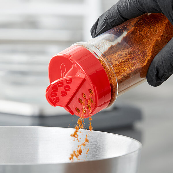 A person pouring seasoning into a container using a red dual flapper spice lid with 7 holes.
