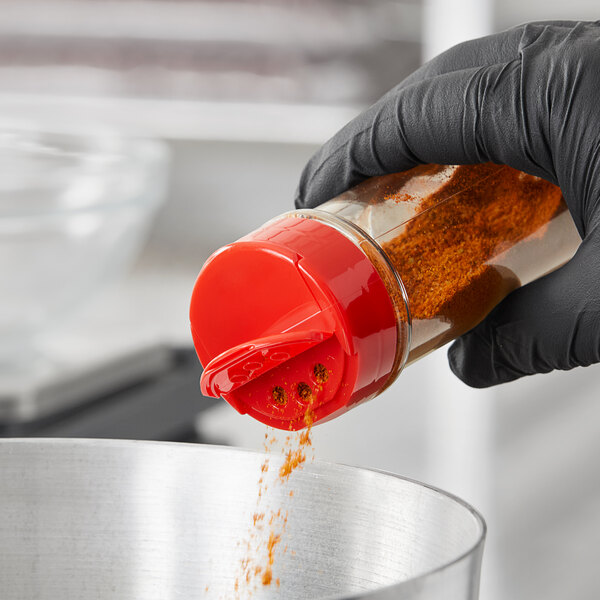 A person in black gloves pouring seasoning into a container using a red 48/485 dual flapper spice lid.