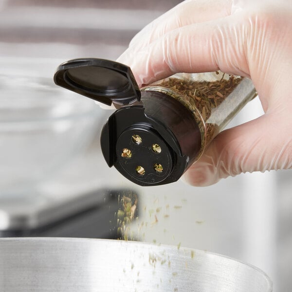 A hand using a 43/485 black flip and sift spice lid to pour herbs into a container.