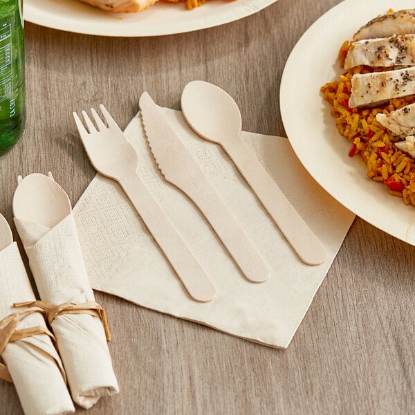 A Hoffmaster FashnPoint napkin and wood cutlery set with wooden forks and spoons on a table with a plate of rice and chicken.