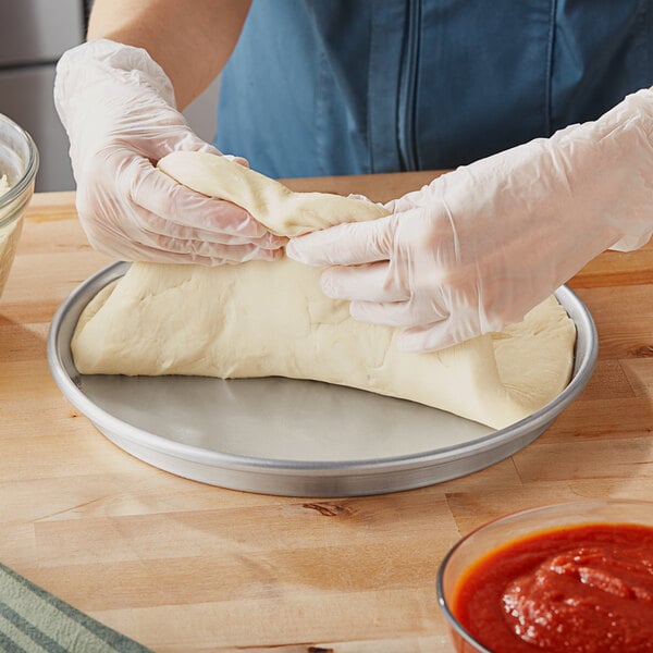 A person in gloves using a Choice Tapered Deep Dish Pizza Pan to make dough