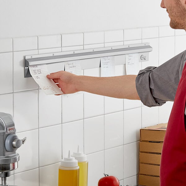 A man in a red apron using a Choice stainless steel wall mounted ticket holder to put a receipt on a wall.