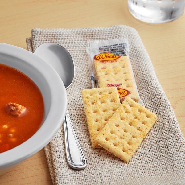A bowl of soup with a Kellogg's Whole Wheat crackers on a table.