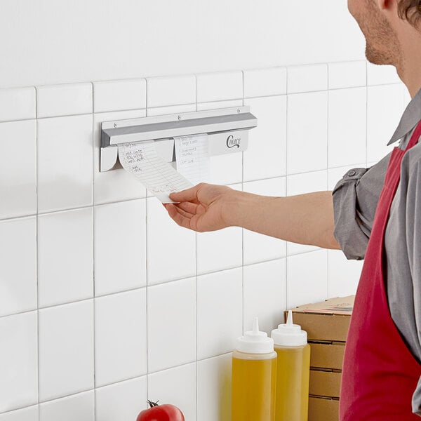 A man in a red apron putting a receipt in a Choice stainless steel wall mounted ticket holder.