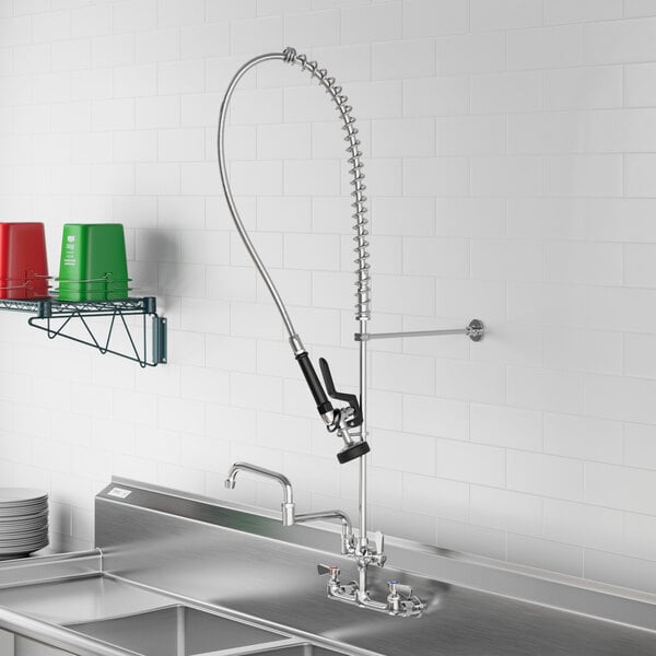 A stainless steel sink with a Regency wall-mounted pre-rinse faucet and a hose.