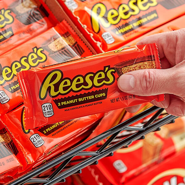 A hand holding a small package of REESE'S Peanut Butter Cups