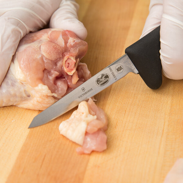 A person in gloves using a Victorinox poultry boning knife to cut chicken on a cutting board.