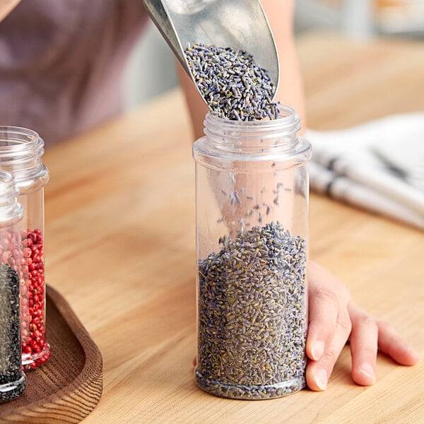 A person pouring lavender seeds into a round plastic spice jar.