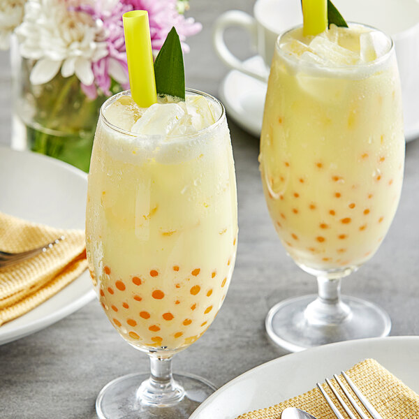 Two glasses of yellow Fanale pineapple milk tea with green straws and leaves.