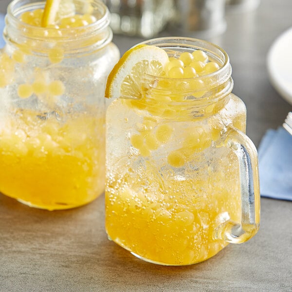 Two mason jars filled with yellow lemonade and ice with Fanale Lemon Popping Boba on a table.