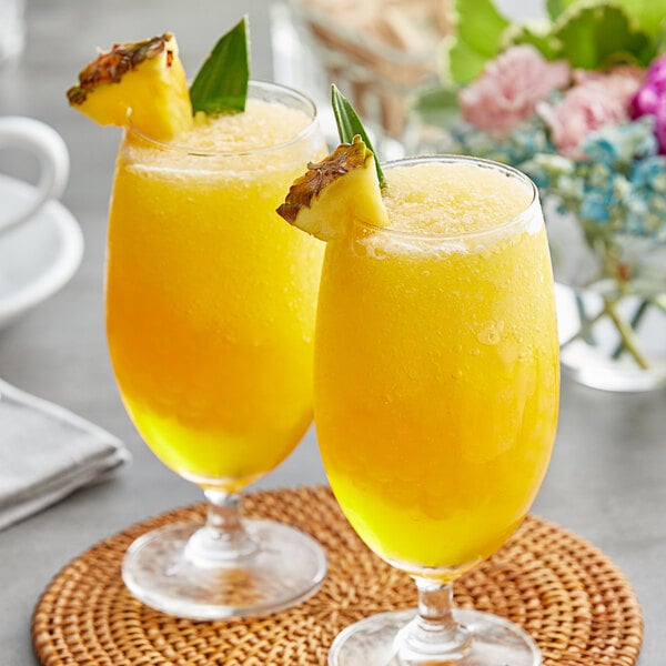 Two glasses of yellow liquid with pineapple slices on top.