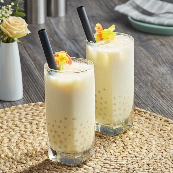 Two glasses of milk tea with yellow Fanale Yogurt Popping Boba on a table.