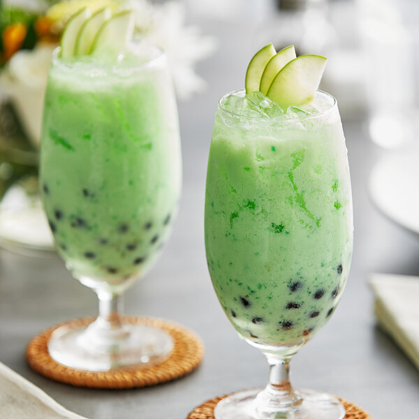 Two glasses of green apple drinks with fruit slices on top.