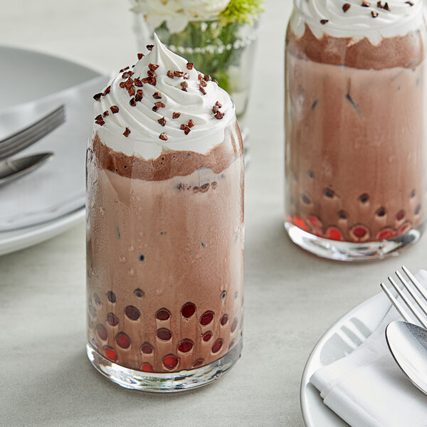 Two glasses of Fanale chocolate milkshake with whipped cream and sprinkles on a table.