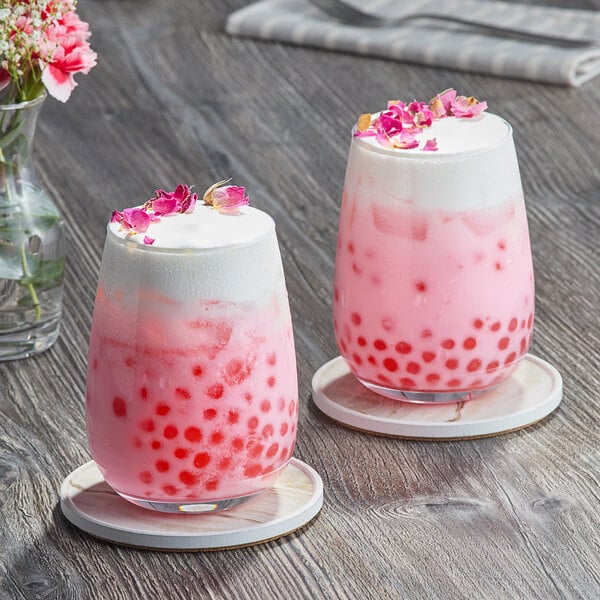 Two glasses of pink and white drinks with pink bubbles and flowers.
