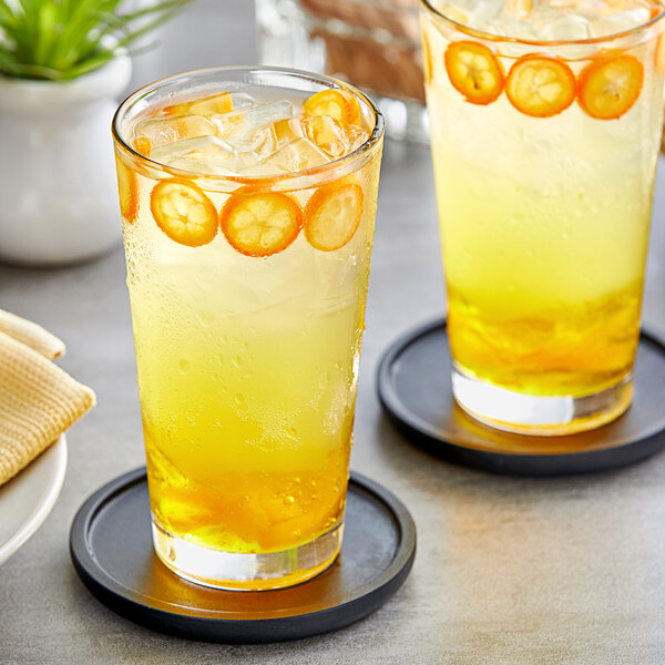 A pair of glasses with orange Fanale Kumquat drinks and ice.