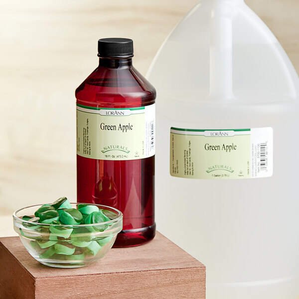 A bottle of LorAnn Oils Green Apple Natural Flavor extract on a counter next to a jug of juice.