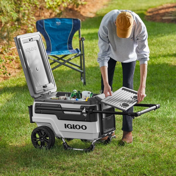 A woman opens a white Igloo Trailmate Journey cooler on the grass.