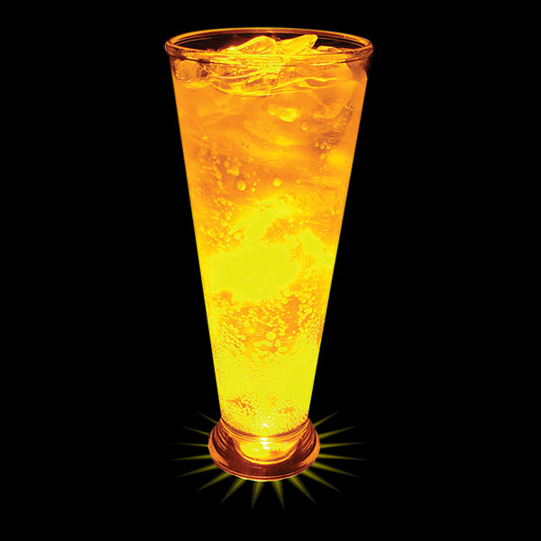 A close-up of a 12 oz. plastic pilsner cup with yellow LED light filled with orange liquid and ice.