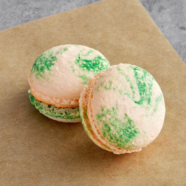 Two Macaron Centrale papaya buttercream macarons with green and white frosting on a brown tray.