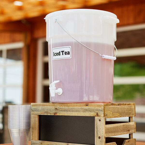 A Cambro plastic container with a white lid and a white handle filled with iced tea on a table outdoors.