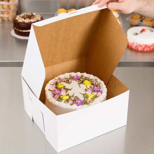 A person holding a 10" x 10" white cake in a customizable box with flowers on it.