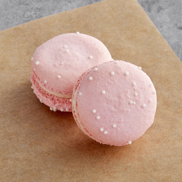 Two pink Macaron Centrale macarons on a brown surface.