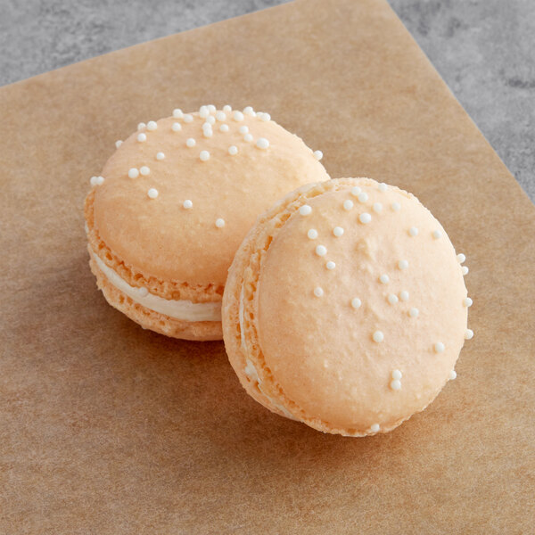 Two Macarons with white sprinkles on top of a brown surface.