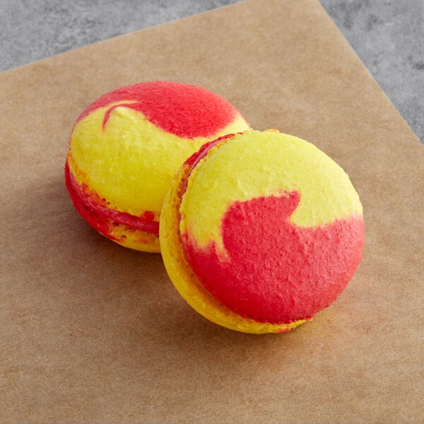 Two yellow and red Macaron Centrale macarons on a brown surface.