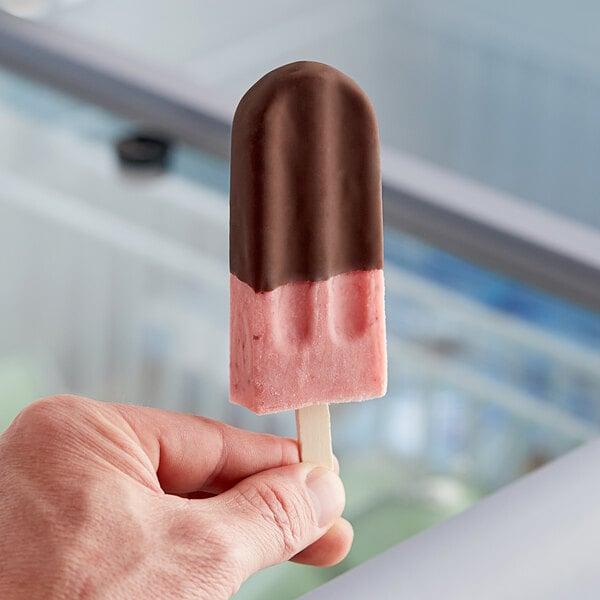 A hand holding a JonnyPops chocolate-dipped strawberry and fresh cream ice cream bar.