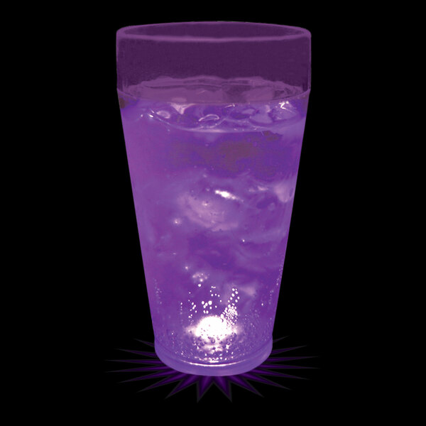 A 20 oz. customizable plastic cup with a purple LED light filled with purple liquid on a bar counter.