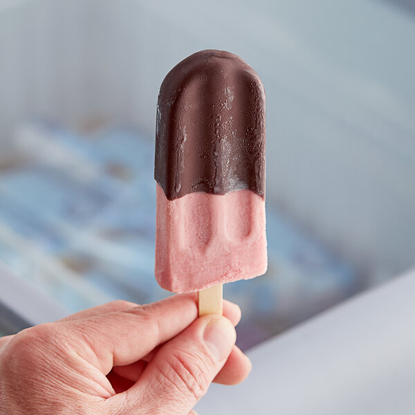 A person's hand holding a JonnyPops chocolate-dipped cherry popsicle.