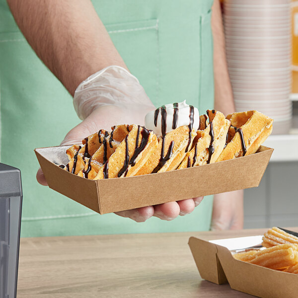 A person holding a tray of waffles in Carnival King medium foiled paper food trays.