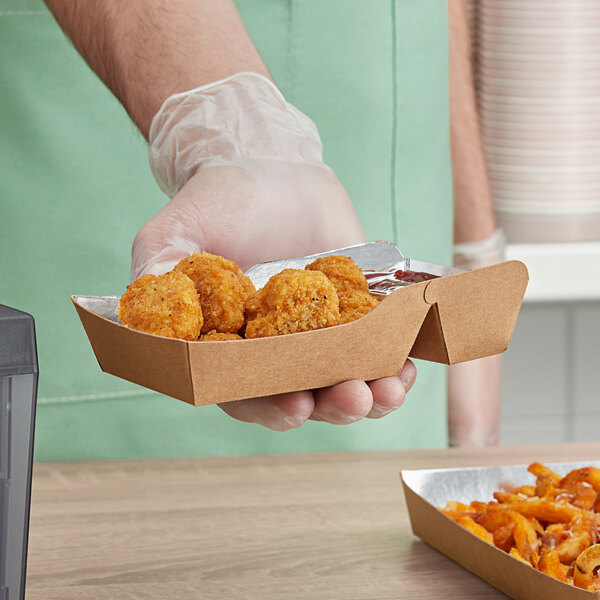 A hand holding a Carnival King small two-compartment paper food tray with fried chicken nuggets and fried chicken.