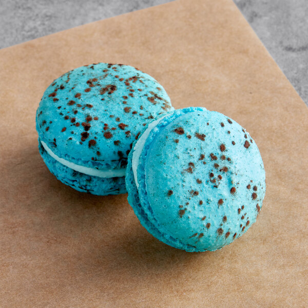 Two blue Macaron Centrale macarons with white chocolate sprinkles on top.