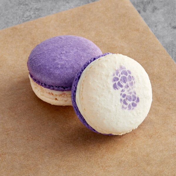 Two purple and white Macaron Centrale blackberry sundae macarons on a brown surface in a bakery display.