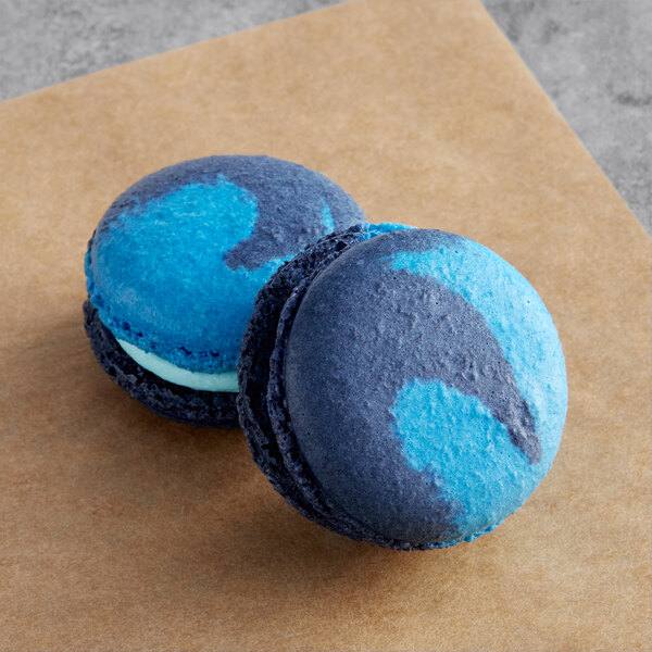 Two blue and black Macaron Centrale macarons on a brown surface.