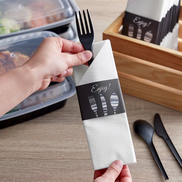 A hand holding a fork in a black Dinex paper napkin.
