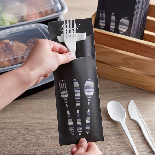 A hand holding a black paper with a fork, spoon, and knife.