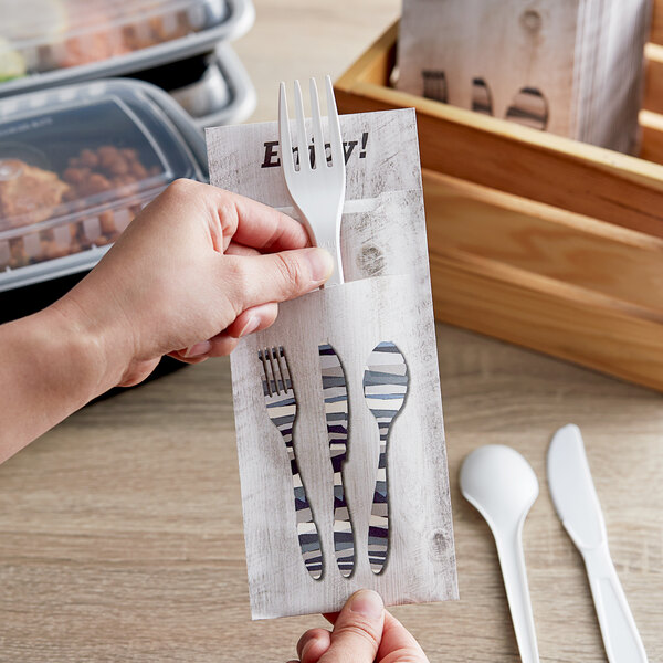 A hand holding a Dinex Woodgrain paper fork and spoon set.