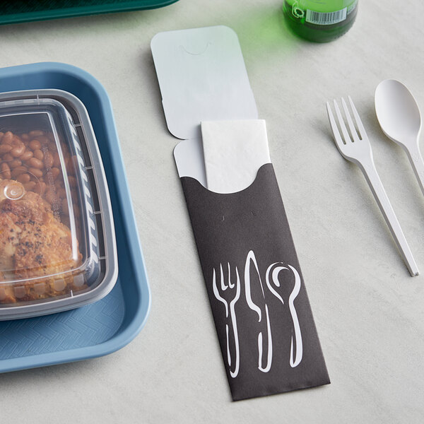 A black paper cutlery caddy with a fork and spoon next to a container of beans and chicken.
